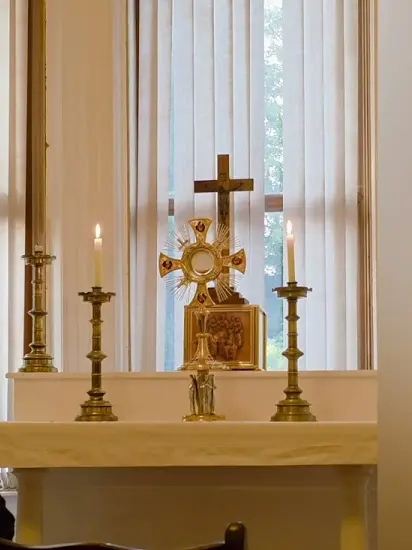 The Blessed Sacrament exposed in a monstrance on the altar, between two lit candles, with a crucifix above