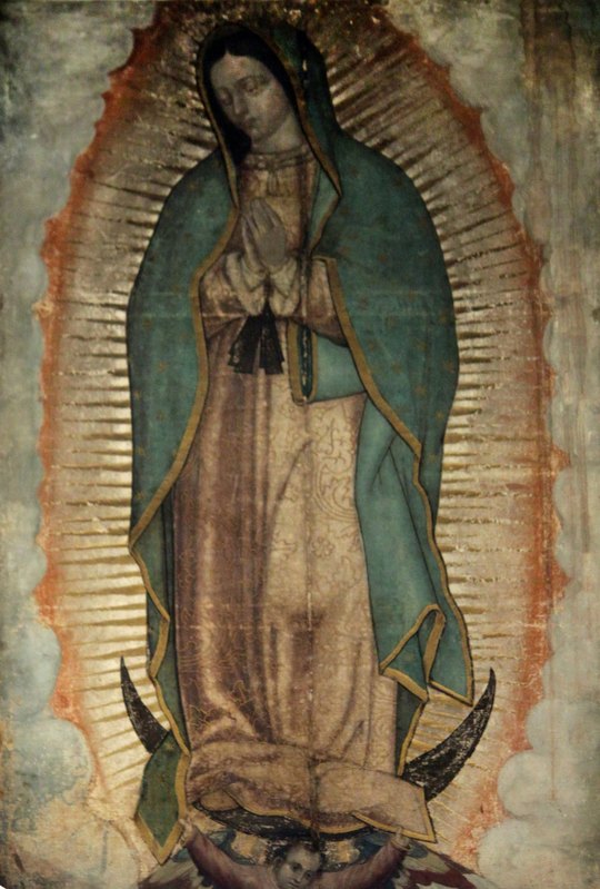A imagem original de Nossa Senhora de Guadalupe, na tilma guardada na Basílica da Cidade do México: a Virgem de mãos postas, com manto verde-azulado e estrelas, cercada de raios, de pé sobre a lua e sustentada por um anjo